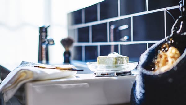 A closeup of a white sink, featuring soap in a bowl and a razor on a towel.