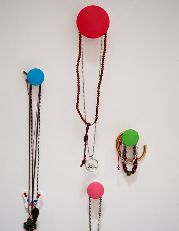 A closeup of colorful IKEA circlular chooks mounted to a white wall, hanging a collection of necklaces and bracelets.