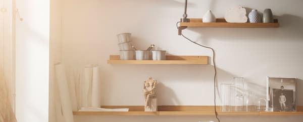 A closeup of four shelves on a wall with decorations, a light and art supplies on the shelves.