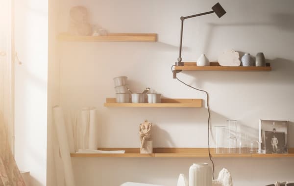 A closeup of four shelves on a wall with decorations, a light and art supplies on the shelves.