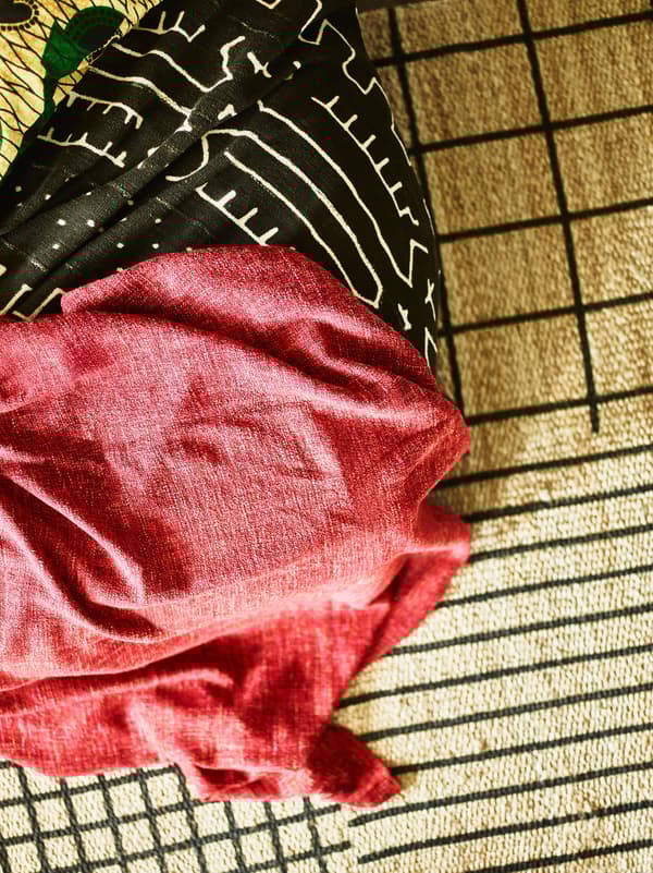 A closeup of layered natural fibre rugs and bright red and textiles help give this bedroom it’s distinctive look.