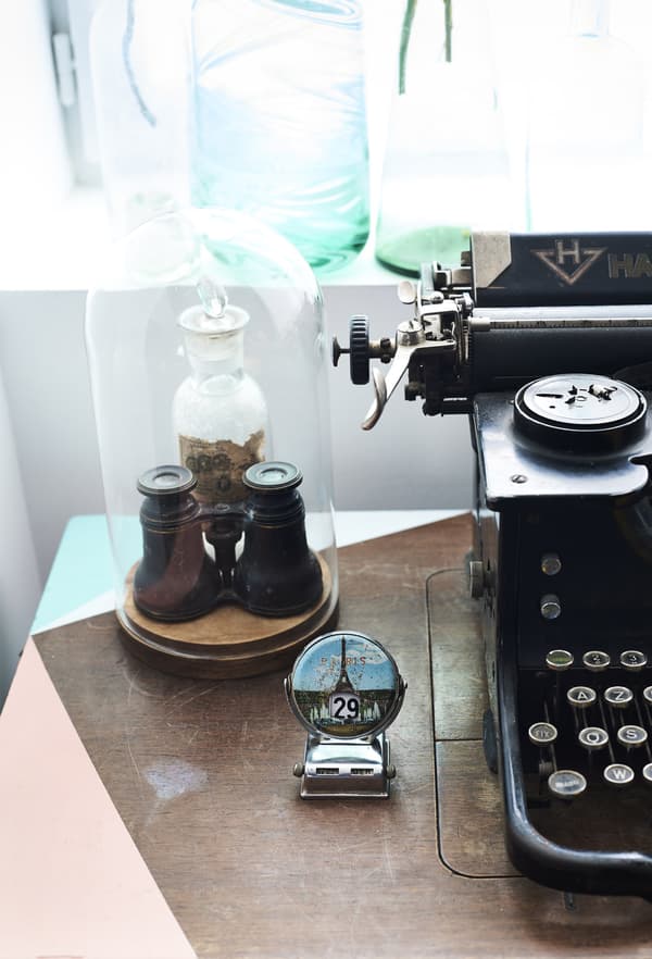 A closeup of tiny binoculars kept safely in an oval-shaped glass display case, next to a vintage typewriter.