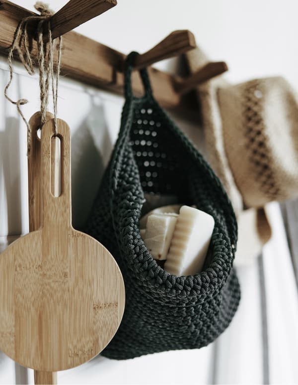 A closeup of wooden hooks mounted to the wall to hang an IKEA NORDRANA woven basket and other wooden accessories.