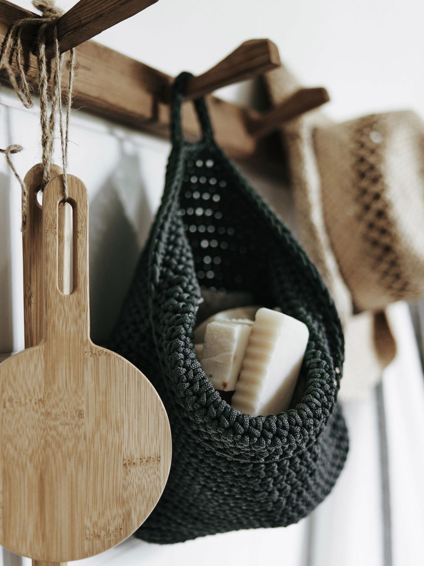 A closeup of wooden hooks mounted to the wall to hang an IKEA NORDRANA woven basket and other wooden accessories.