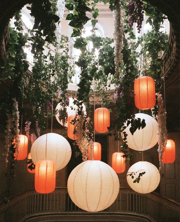 A cluster of flowers and pendant lamps with white and pink paper shades hanging in a hallway.