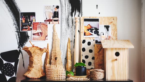 A cluster of objects including a black KONSTFULL vase sit on a flat surface in front of images taped to a wall.
