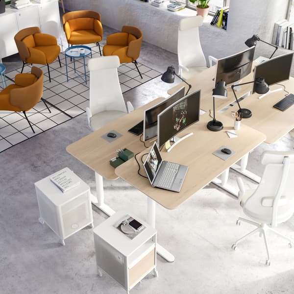 A co-working office showing an area for lounging with yellow armchairs, and four desks arranged together.