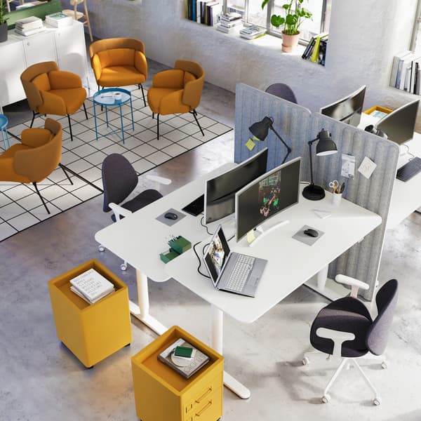 A co-working office showing an area for lounging with yellow armchairs, and four desks arranged together.