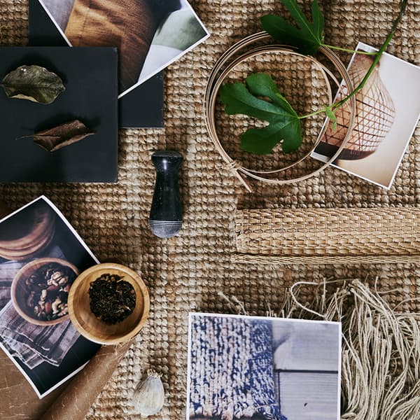 A coarsely woven rug with several printed pictures plus a variety of raw materials including leaves and wool.