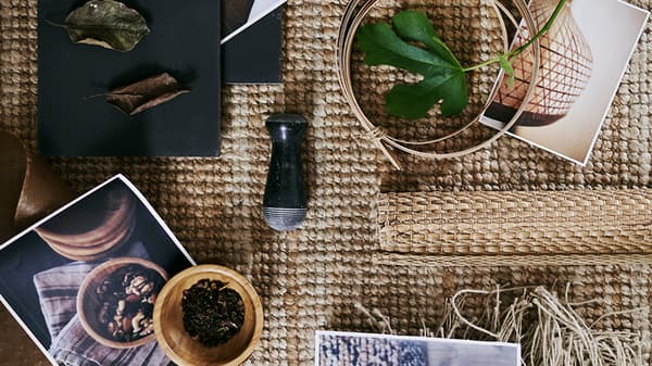 A coarsely woven rug with several printed pictures plus a variety of raw materials including leaves and wool.