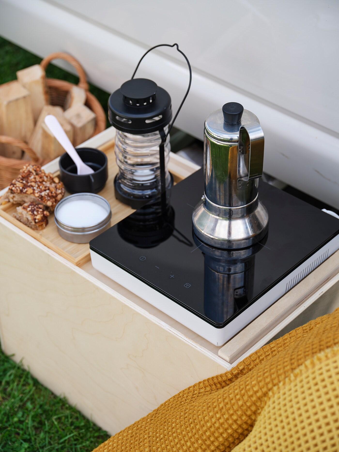 A coffee maker sitting on top of the TILLREDA portable induction hub with a solar lantern next to it