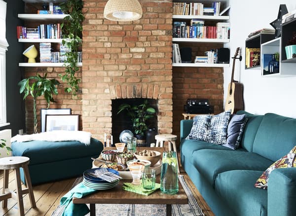 A coffee table set with food in a living room with a green sofa and red brick wall.