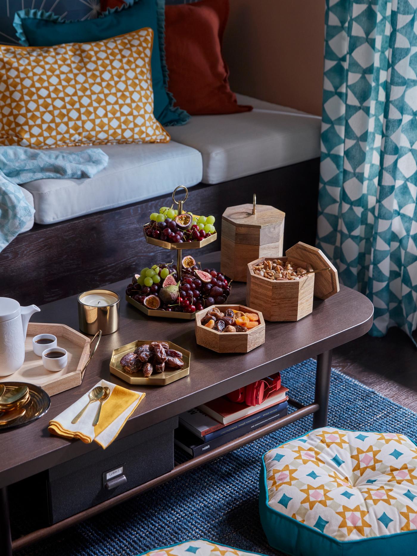 A coffee table with GOKVÄLLÅ products on it, like serving trays, kava cups, boxes with lid, and a serving stand with fruit.