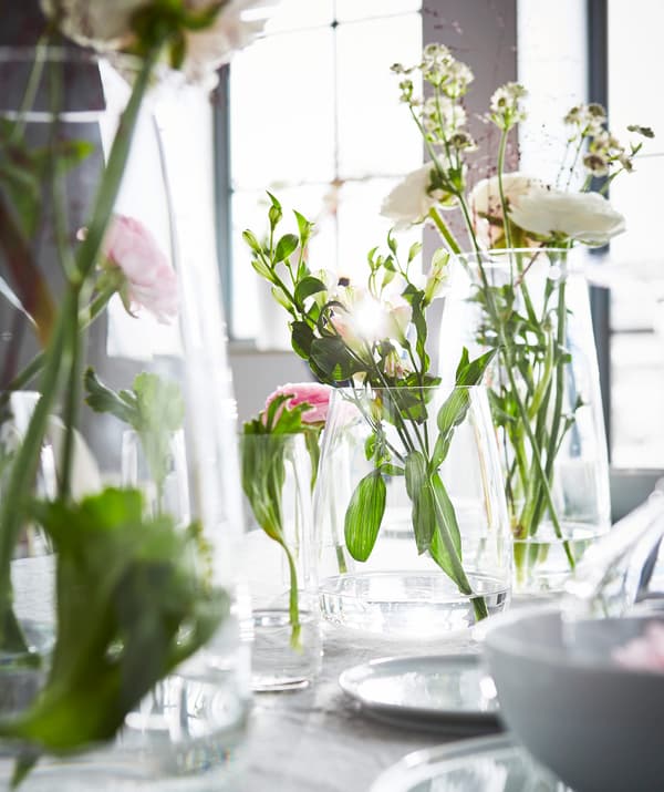 A collection of clear glass vases with flower arrangements on a dining room table.
