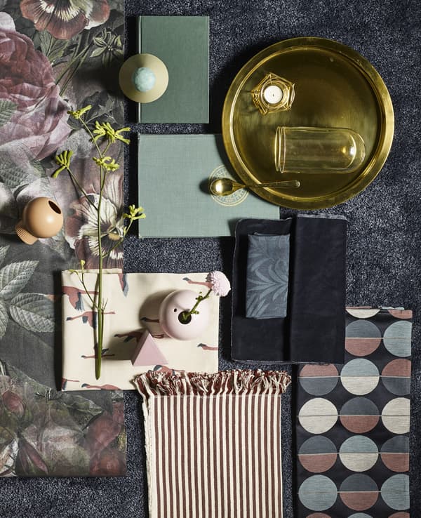 A collection of home décor in greens, pinks, and brass colour, set on a rectangular ÅDUM rug in dark blue.