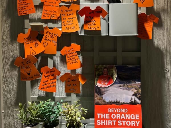 A collection of orange shirt papers are pasted to a board hanging on a wall.
