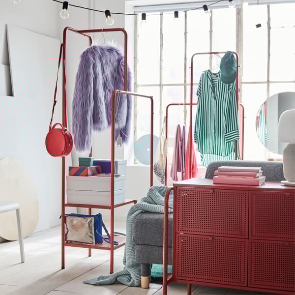 A colorful bedroom with two red clothes rack where clothes hang, and storage boxes are placed on the bottom shelves.
