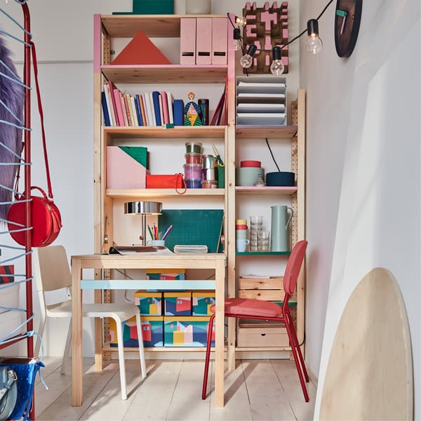 A colorful bedroom work/dining area with a foldable table in pine that's paired with red and white chairs.