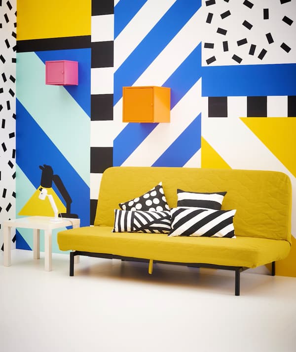 A colorful graphic print room with a yellow sofa bed and pink and orange storage cubes on the wall.