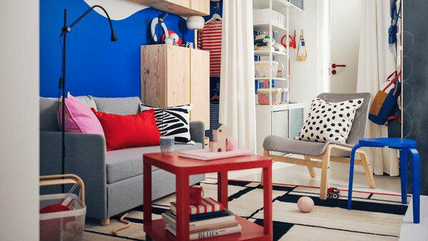 A colorful livingroom space featurong a grey couch, red and blue furniture items and various pillows