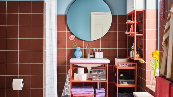 A colourful bathroom with a wash-basin unit, shelf and trolley in red-orange steel and a round mirror.