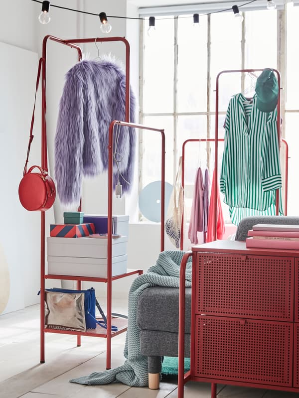 A colourful bedroom with two red IKEA NIKKEBY clothes racks with hanging clothes, storage boxes are placed on the bottom shelves.