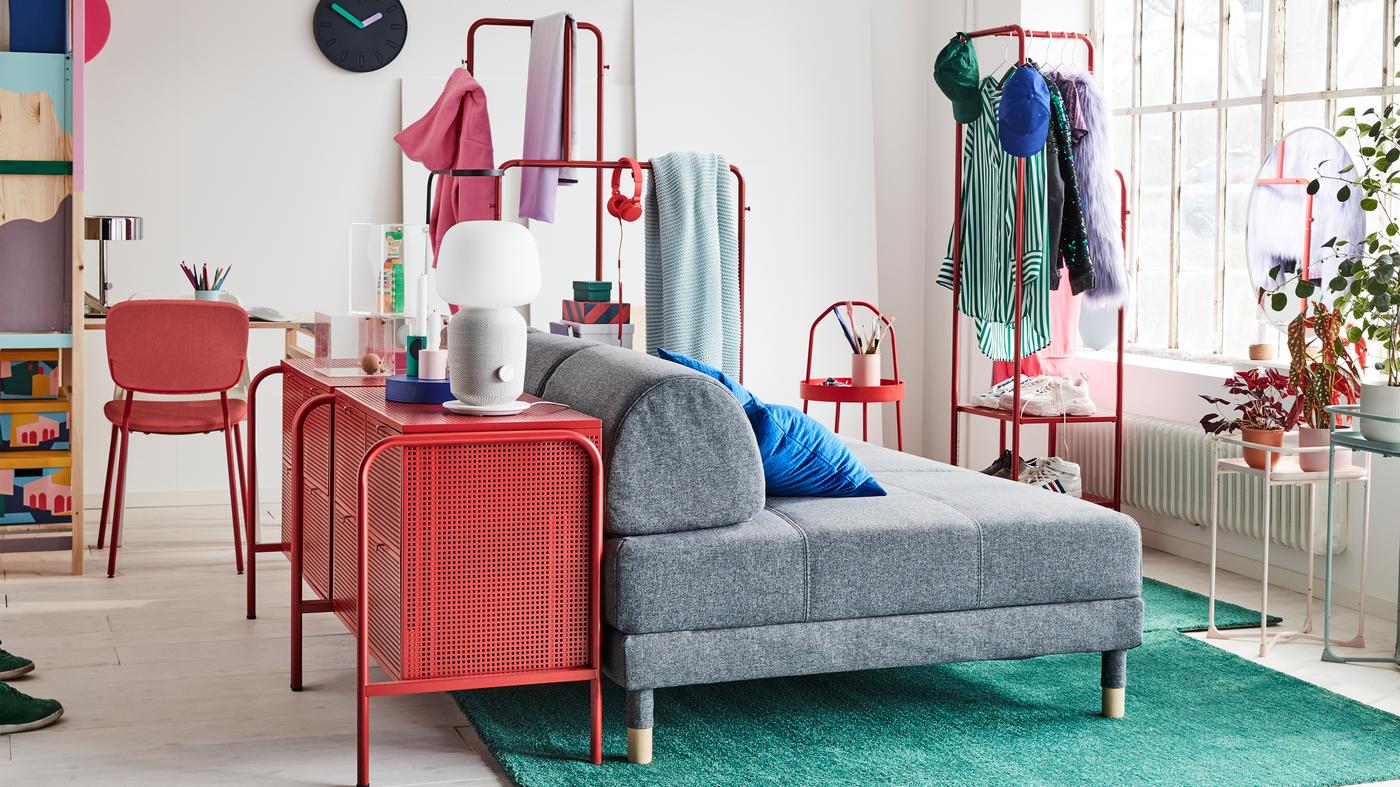 A colourful one-bedroom-apartment with a grey sofa bed, two green rugs and two red chest of drawers.