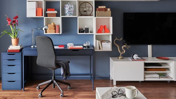 A complete home office setup with a desk, ergonomic chair, TV, and modular wall-mounted shelves.