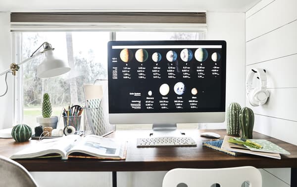 A computer monitor on a desk with notepads, files and a lamp.