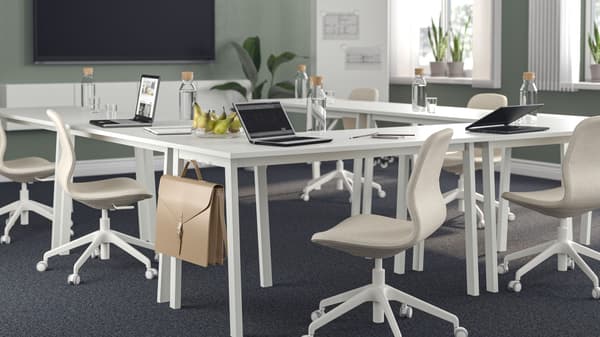 A conference room with tables, chairs, and a TV on the wall.