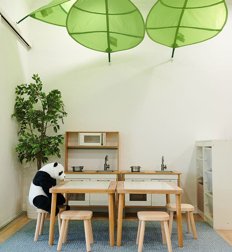A cook and eat play area featuring play kitchens, wooden tables and stools.