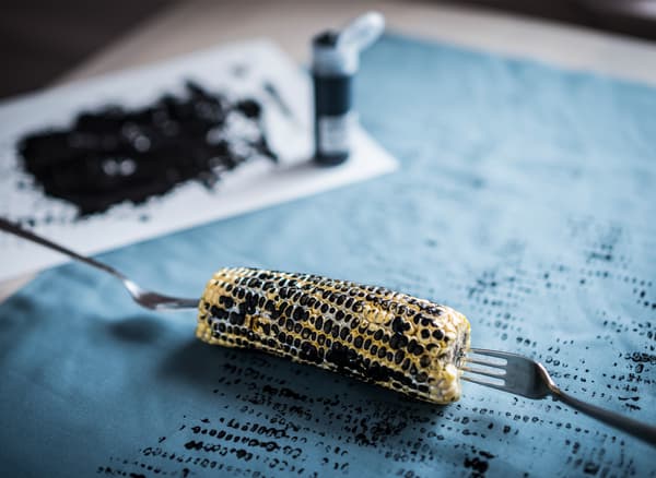 A corncob pinned with forks and rolled across blue fabric with black paint.