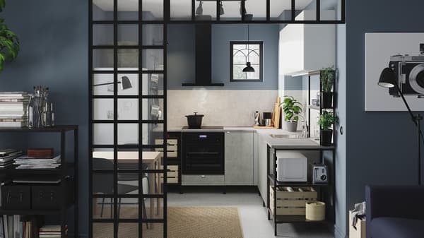 A corner kitchen in anthracite/concrete effect/white with open and closed storage, black lamps, herbs in pots and a jute rug.