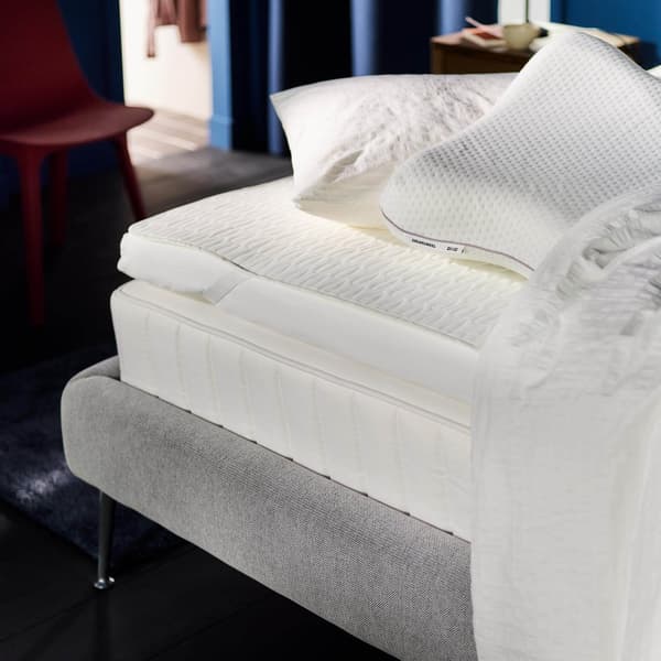 A corner of a bed showing a white mattress with bedding on it.