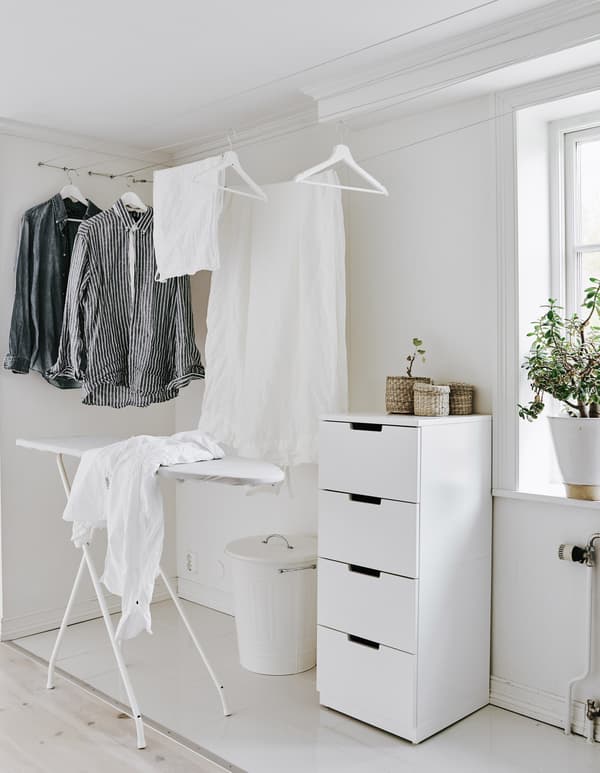 A corner of a home turned into a small laundry area, including clothes rails to hang dry clothes and a white ironing board.