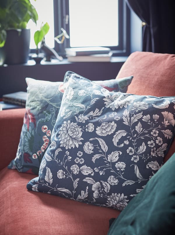 A corner of a red GRÖNLID sofa with three cushions nestled together: one in an IDALINNEA cover and the other in similar colours.