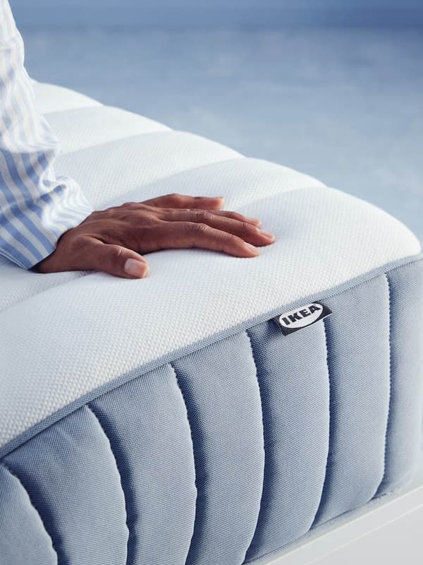A corner of a VALEVÅG pocket sprung mattress with a person’s hand resting on the top surface of the mattress.