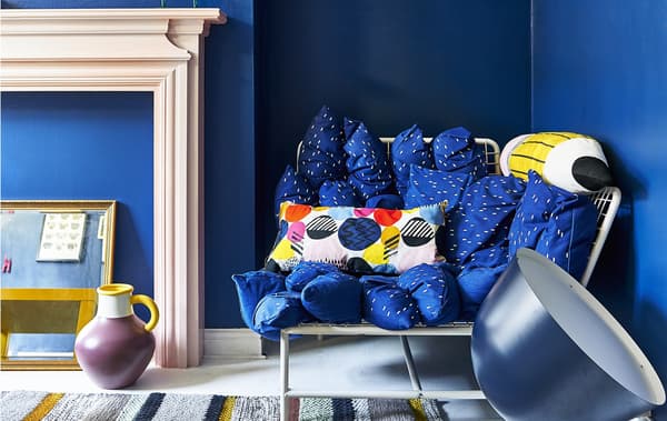 A corner sofa with white metal frame filled with lots of blue scatter cushions against navy blue walls.