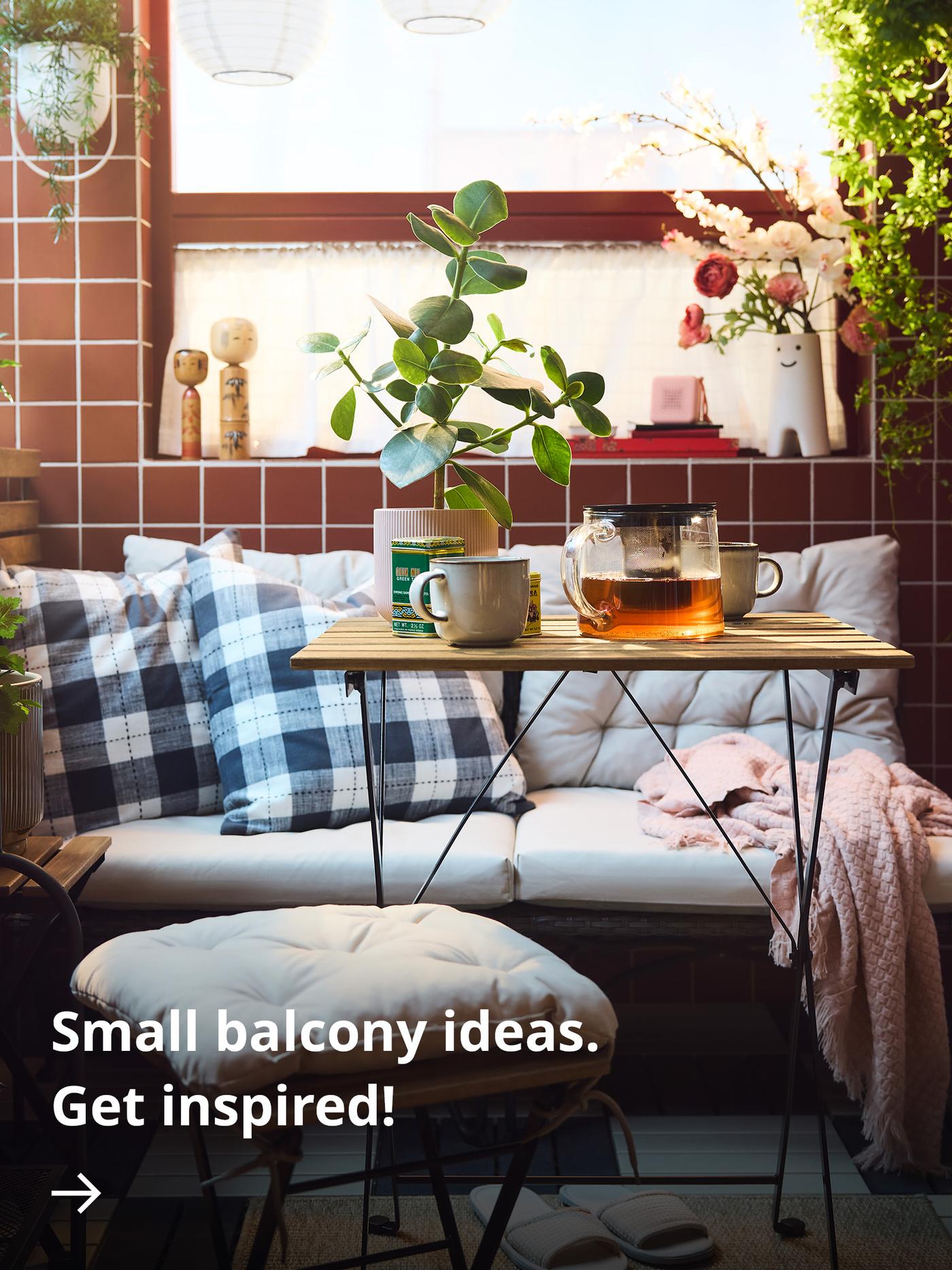 A cosy balcony with red tiles, checkered cushions on a bench, a small wooden table with mugs and a glass teapot, and potted plants in soft sunlight.