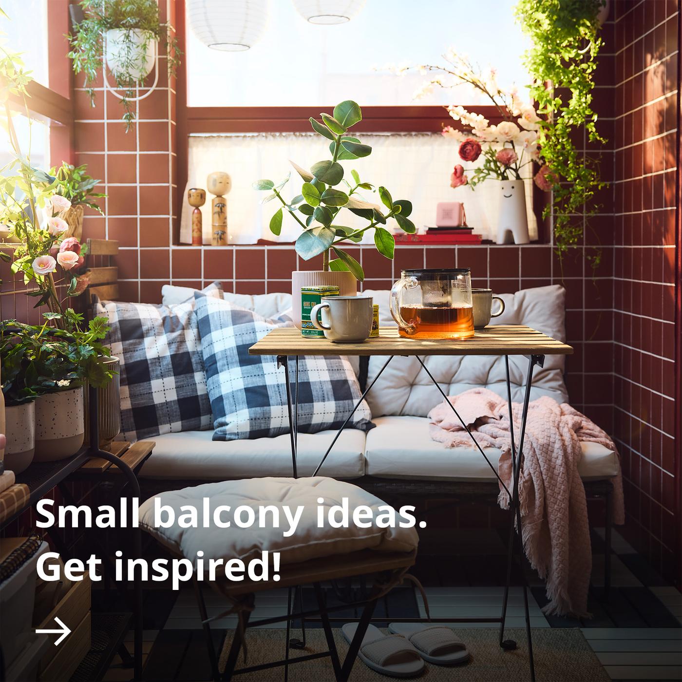A cosy balcony with red tiles, checkered cushions on a bench, a small wooden table with mugs and a glass teapot, and potted plants in soft sunlight.