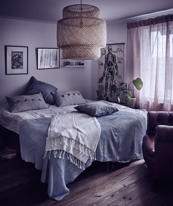 A cosy bedroom with grey walls and grey and blue cushions and throws on the bed, and a rattan pendant lamp.