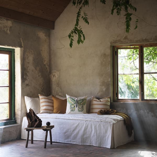 A cosy corner with windows features a daybed with striped brown cushions and a RÖTFJÄRIL butterfly cushion in the middle.