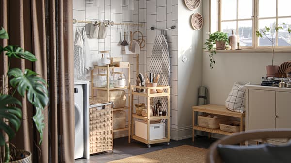 A cosy laundry nook with dark beige DYTÅG curtains as a room divider and RÅGRUND trolley and storage shelf in natural bamboo.