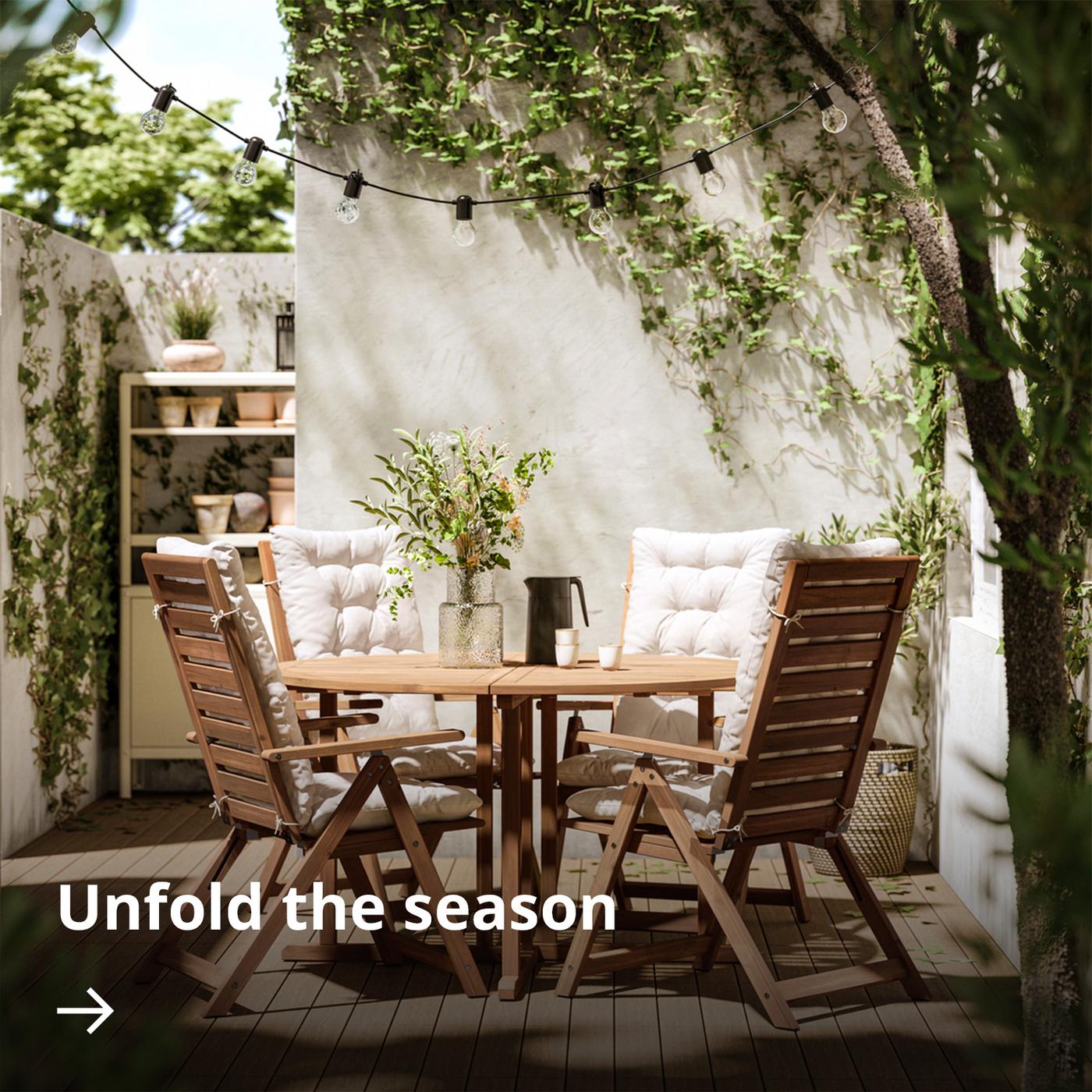 A cosy outdoor patio with a round NÄMMARÖ table, surrounded by cushioned reclining chairs made from acacia wood.