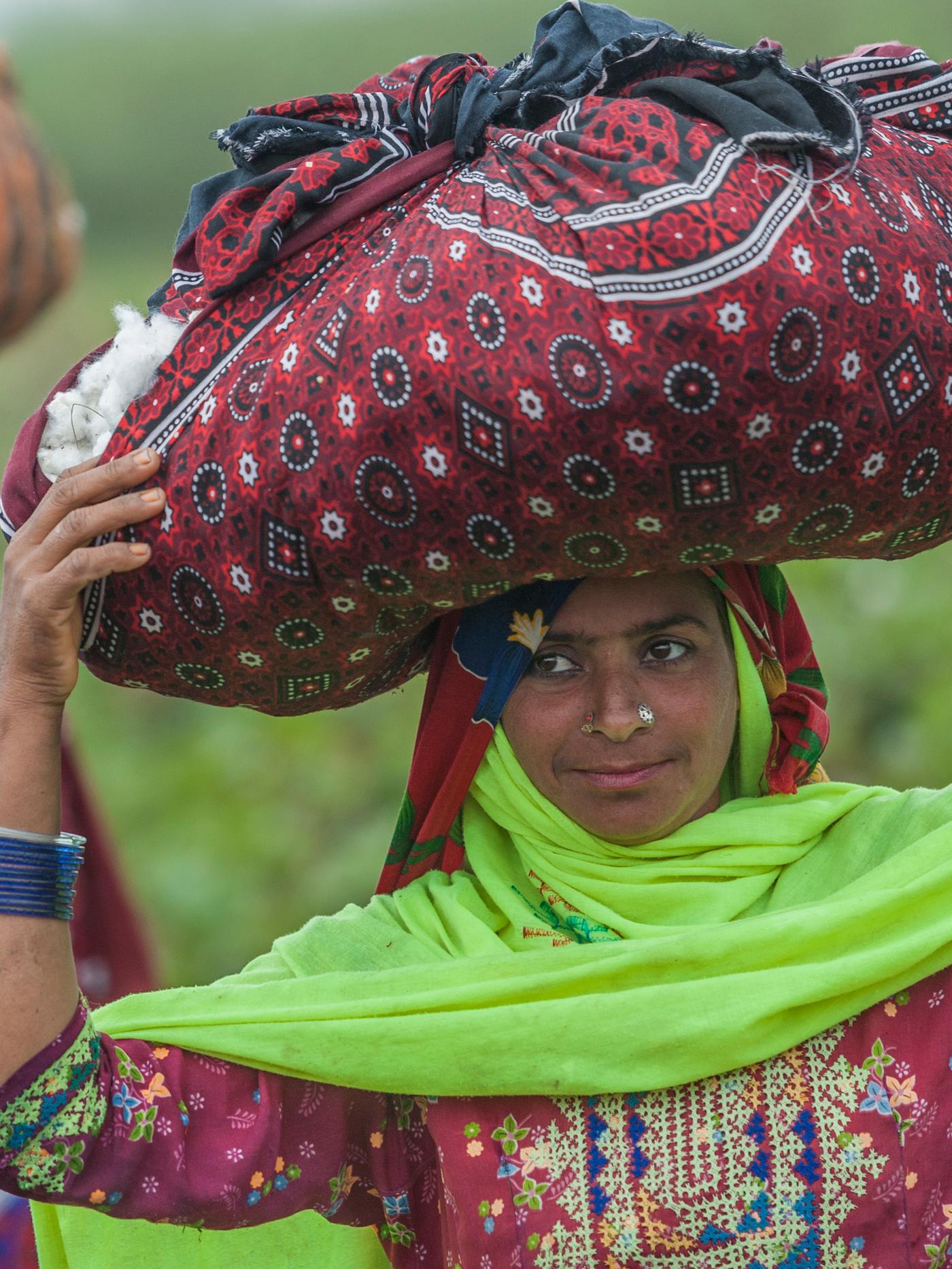 A cotton picker dressed in brightly coloured clothes carrying a bundle of picked cotton wrapped in a large cloth.