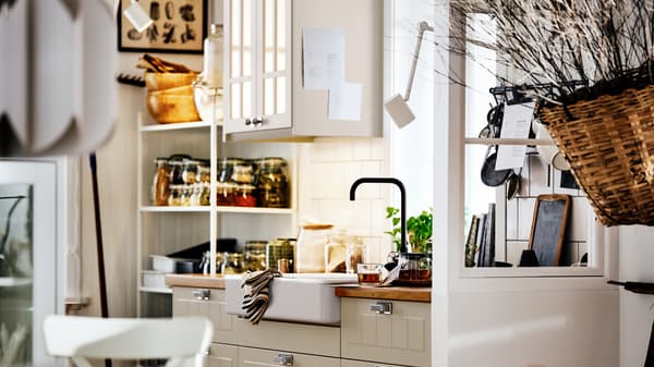 A country-style kitchen with beige STENSUND fronts on METOD cabinets, with a white HAVSEN sink and shelving holding jars.
