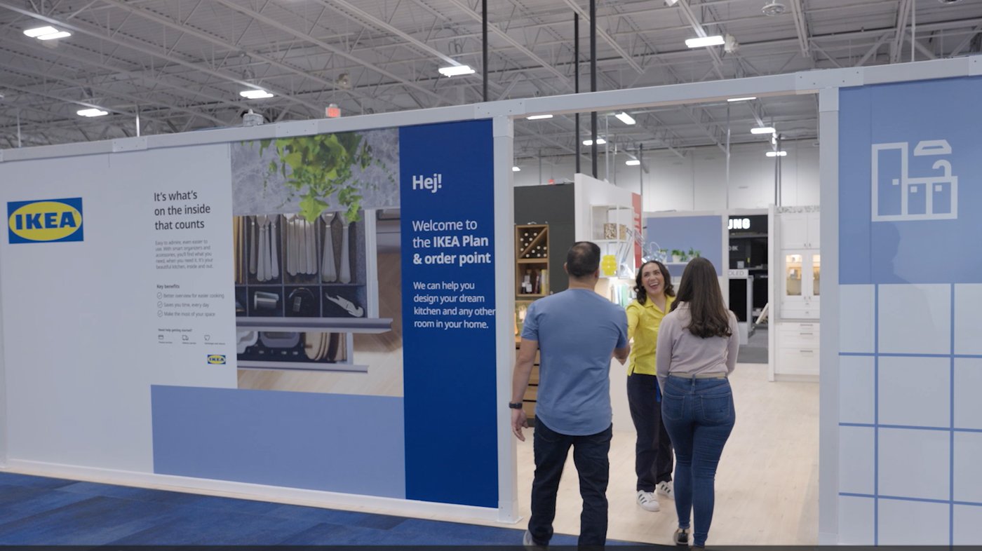 A couple and a coworker walk around an IKEA planning center inside a Best Buy store.