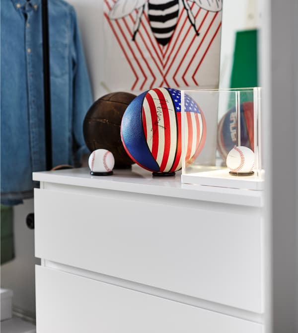 A couple of baseballs and basketballs sit on top of a white chest of drawers.