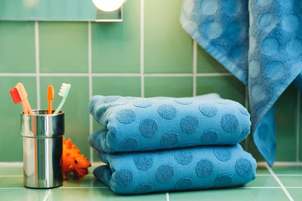 A couple of folded blue MÅLSELVA towels and a KALKGRUND toothbrush holder placed on green tiles.