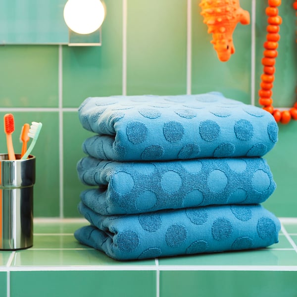 A couple of folded blue MÅLSELVA towels and a KALKGRUND toothbrush holder placed on green tiles.